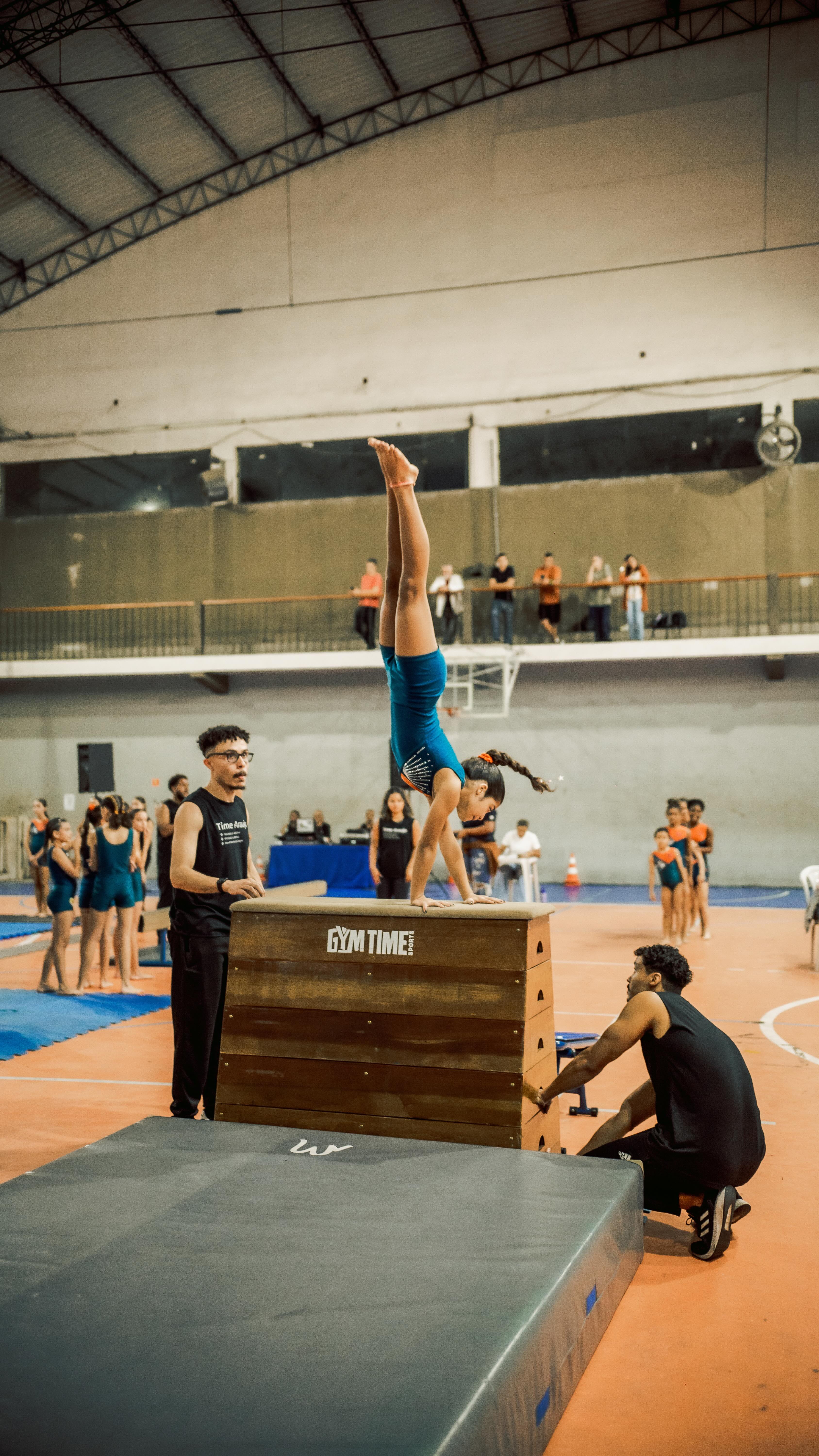 Aluna de ginástica artística praticando com acompanhamento da equipe
